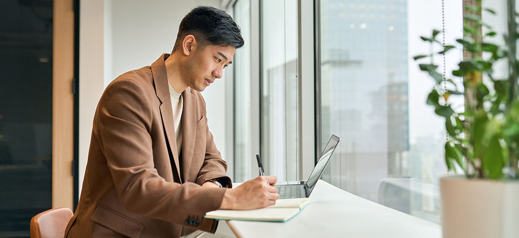Man working with his laptop and notebook in front of large windows