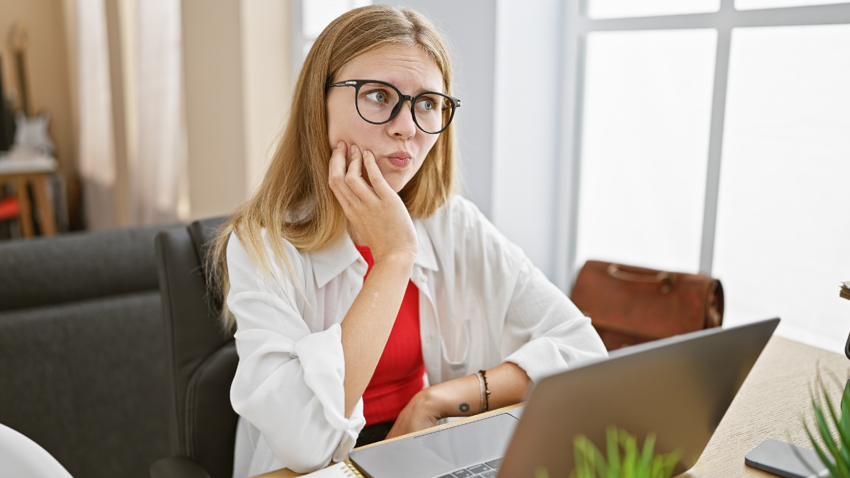 Woman in a red shirt, sitting in front of a computer, worrying.