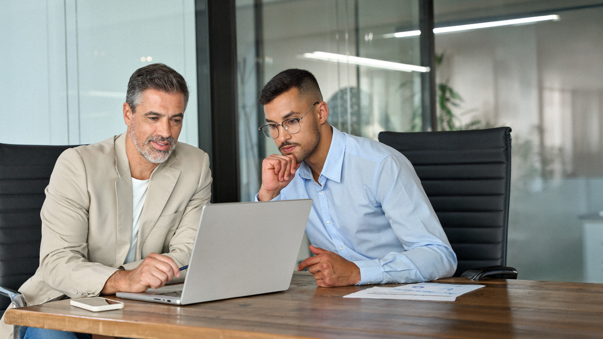 Senior manager and younger professional reviewing laptop together at conference room table